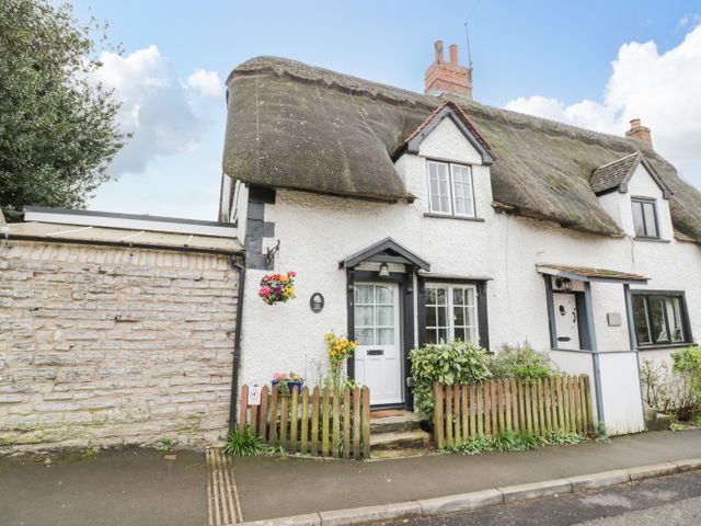 Thatched roof cottage with white walls small wooden fence and flowers outside at Apple Tree Cottage in Harvington