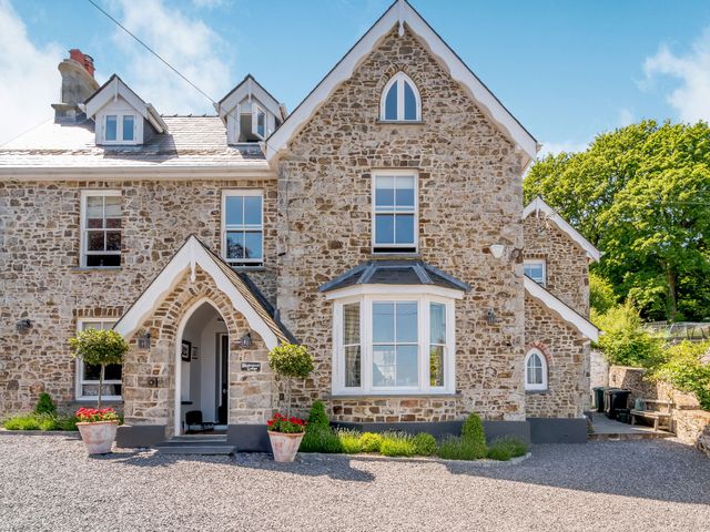 A stone house with an arched entrance and potted plants in front at Rhodewood Lodge in Saundersfoot