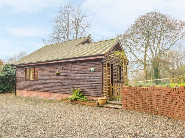 An exterior view of a wooden cottage with a gravel driveway and a brick wall at Woodpeckers Cottage in Church Stretton