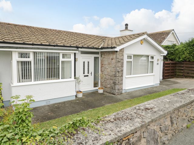 Exterior of a single story house with white walls stone detail and a paved walkway at Moranva in Benllech near Red Wharf Bay