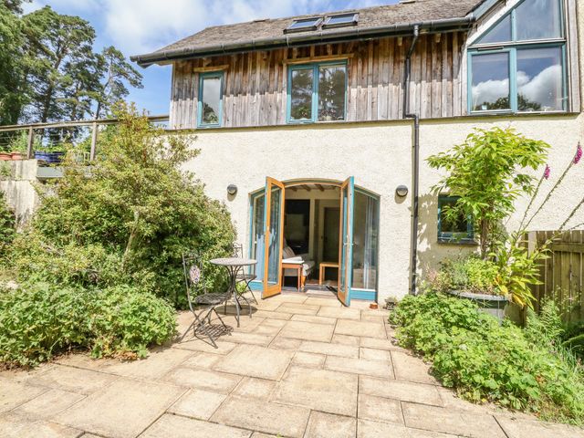 A patio with a small round table and two chairs outside a house with open double doors and surrounding plants at The Garden Flat in Torlundy near Fort William