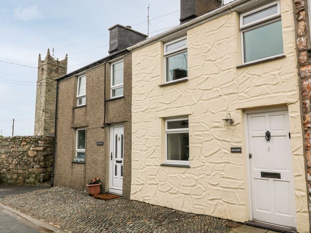 A street view of two adjoining houses with pebble stone pavement and a stone tower in the background at Haddef in Nefyn