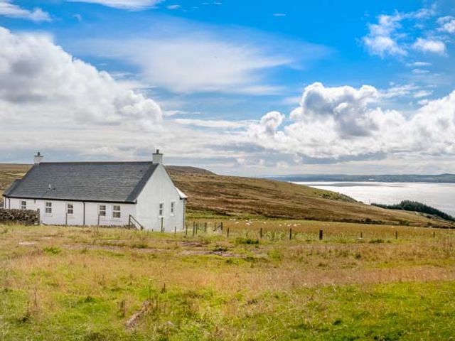 A white house on a grassy hillside with a view of water and hills at Little Laight in Cairnryan near Stranraer