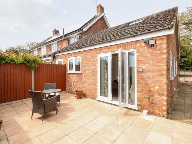 A small outdoor patio with two wicker chairs and a round table next to a brick house with an open glass door at Highfield in Roughton near Cromer