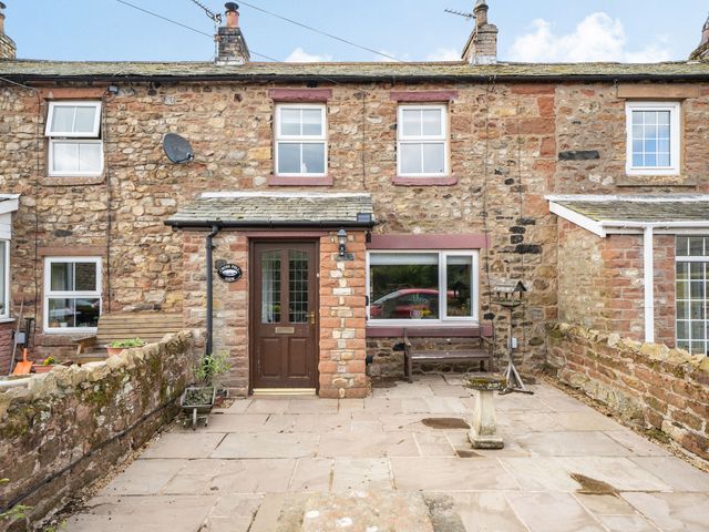 A stone terrace with seating and a bird feeder in front of a stone house at Cross Fell View in Knock near Appleby-in-Westmorland