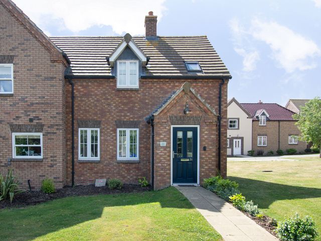 A brick house with a blue front door and white windows with a garden and pathway in front at Lilipad Cottage The Bay near Filey