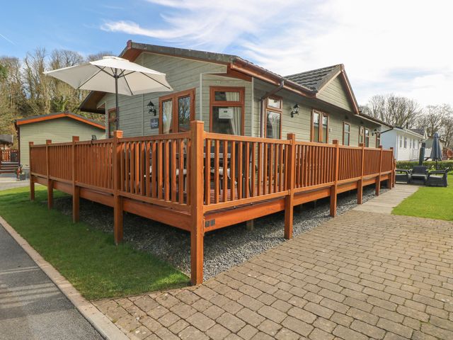 A wooden deck with railing and a white patio umbrella outside a single story cabin at Heddwch Wisemans Bridge near Saundersfoot