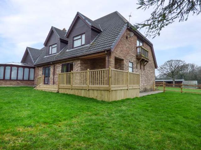 A brick house with a tiled roof wooden deck and green lawn at Cwm Gran Meadows in Llanharry