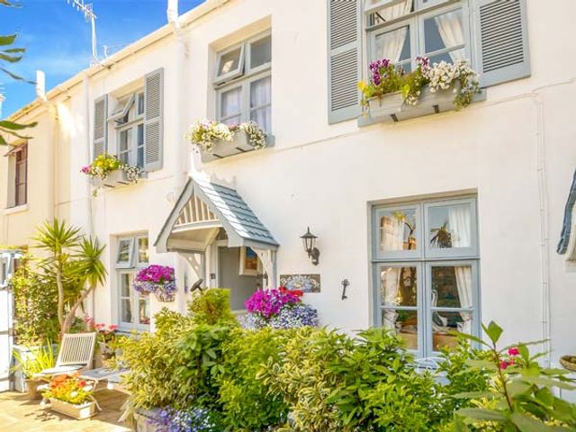 The exterior of a white house with windows flower boxes and a small porch surrounded by plants and outdoor furniture at Blue Harbour Cottage in Torquay