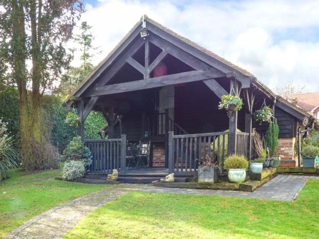 A wooden cabin with a porch and potted plants on a grassy lawn at Studio at Little Trees Farm in Harpenden