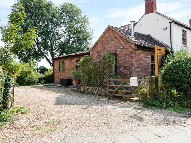 A small brick building with a gravel driveway a wooden gate and trees at The Ramblers Annex in Mattishall