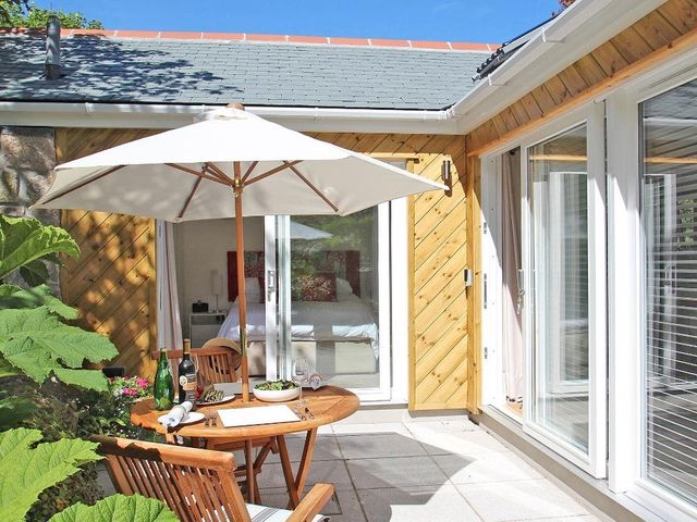 Outdoor patio area with wooden table chairs and umbrella next to sliding glass doors at Cot Valley Cottage in St Just