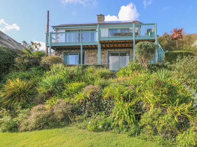 A stone house with blue wooden balconies and greenery in front at Harbour Lights in Mousehole
