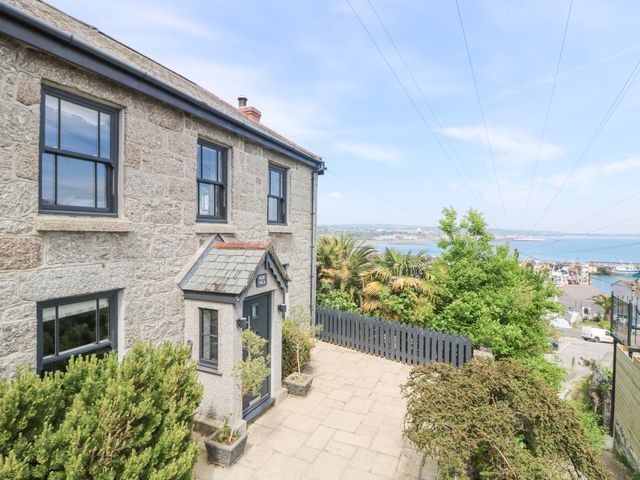 Stone house with three windows and a door with plants outside overlooking a view of trees water and boats at Rose Villa in Newlyn