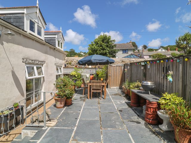A patio with wooden table and chairs under an umbrella and potted plants along a stone path at Ebenezer Cottage in Marazion
