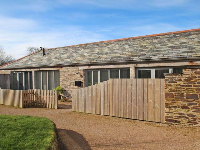 A stone building with a tiled roof and wooden fencing in front at The Old Dairy in Padstow