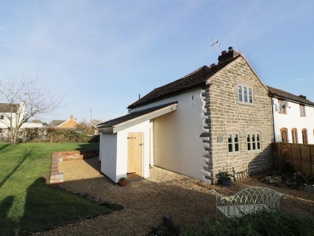 An outdoor area with a stone and white plastered house a gravel pathway a small wooden door a brick retaining wall and a metal bench at Ivy Cottage in Coombe Green Common near Malvern