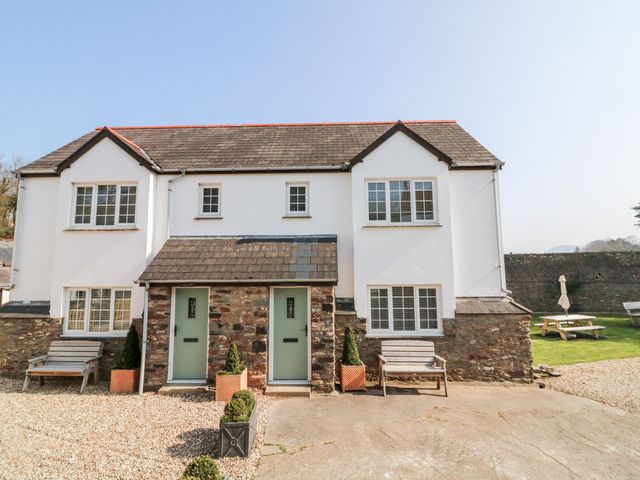 Two story semi detached house with stone and white exterior green doors two benches and potted plants in front at Kingfisher Cottage in Ilfracombe