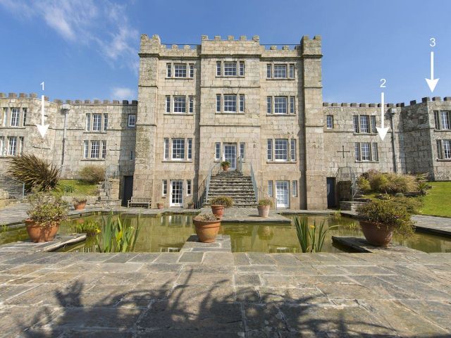 Stone castle-style building with multiple windows and a central staircase leading to a pond with potted plants at Susannas Apartment in Rosudgeon