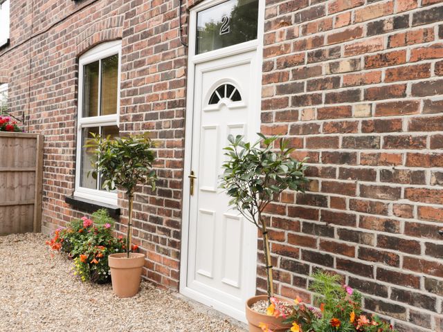 A brick house exterior with a white door numbered 2 two potted plants and flower beds at 2 Moor Farm Cottages Hornsea