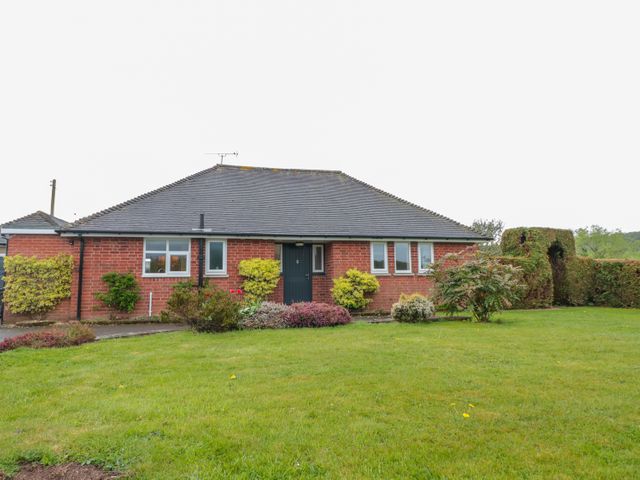 A single-story brick house with a dark roof surrounded by shrubs and grass at Bower View in Madley