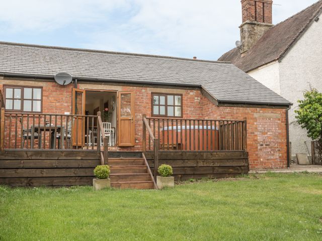 A brick building with wooden deck railing and stairs leading to a green lawn at Old Hall Barn 1 Church Stretton