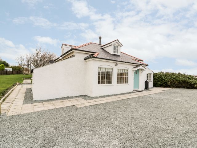 A white house with a blue door and two dormer windows a gravel driveway and paved walkway at Pentowyn in Holyhead