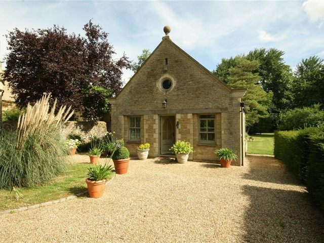 A small stone cottage with potted plants outside and a gravel driveway at Garden Cottage in Black Bourton near Burford