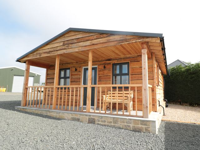 A wooden cabin with a porch and a bench outside in a gravel area at Aln in Longframlington
