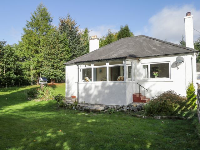 A small white house with a porch and steps surrounded by grass and trees at St Aethans in Bonar Bridge