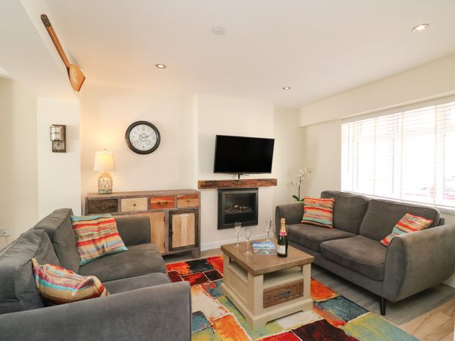 A living room with two gray sofas a colorful rug a wooden coffee table and a wall-mounted television at Anchor Cottage in Brewers Quay Harbour