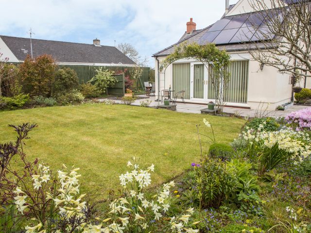 A garden with a lawn flower beds and outdoor seating area near a house with solar panels and sliding doors at The Swallows in Dinas Cross