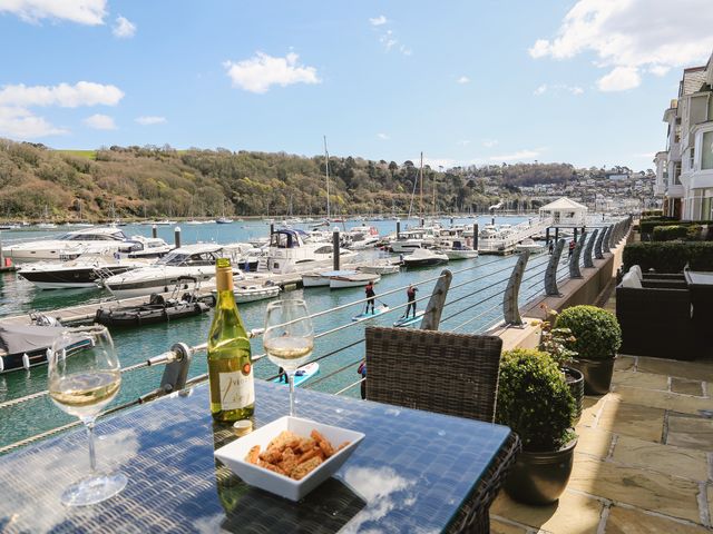 A marina with boats docked and people paddleboarding seen from a terrace with a table holding wine glasses bottle and a bowl at Quayside Dart Marina in Dartmouth
