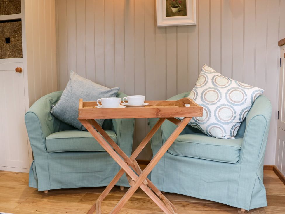 Two light blue armchairs with cushions and a wooden tray table with two cups in a room at Little Silver Leaf in High Bickington