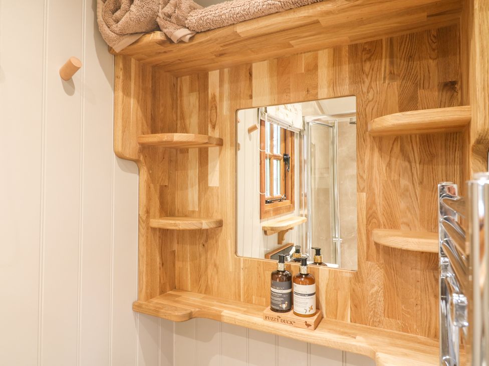 A wooden framed mirror with shelves and toiletries in a bathroom at Little Silver Leaf in High Bickington