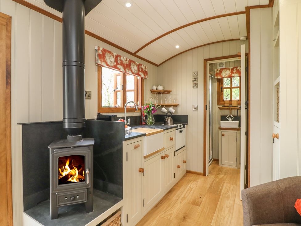 A compact kitchen with a wood stove and a sink next to a doorway leading to a small bathroom at Little Silver Owl in High Bickington