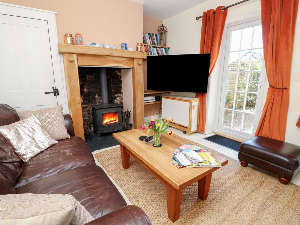 A living room with a brown leather sofa a wooden coffee table with flowers a wood burning stove and a television at 7 Coastguard Cottages in Bognor Regis