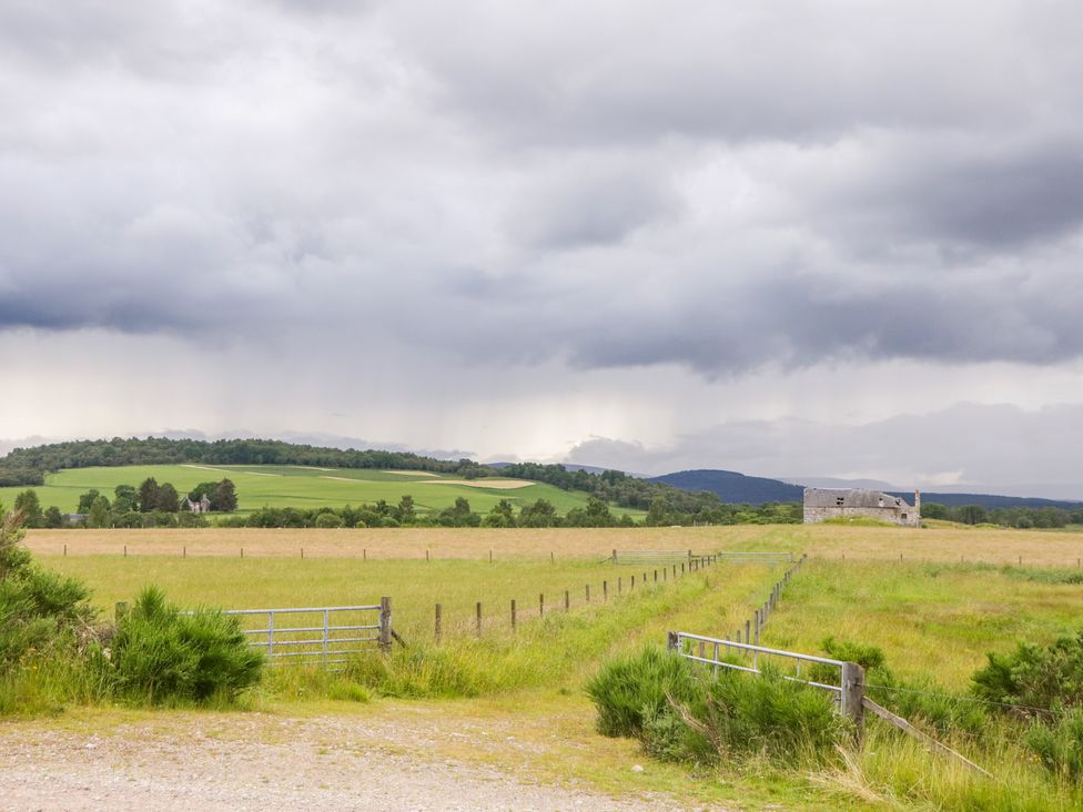 A field with fencing and an old stone building under a cloudy sky at Ptarmigan in Carrbridge