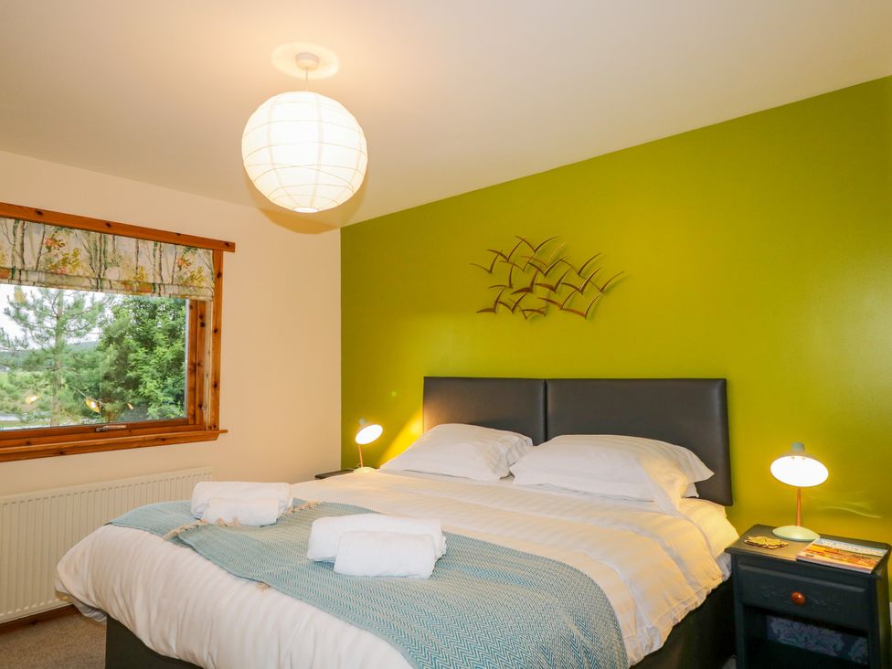 A bedroom with a double bed and green accent wall at Ptarmigan in Carrbridge