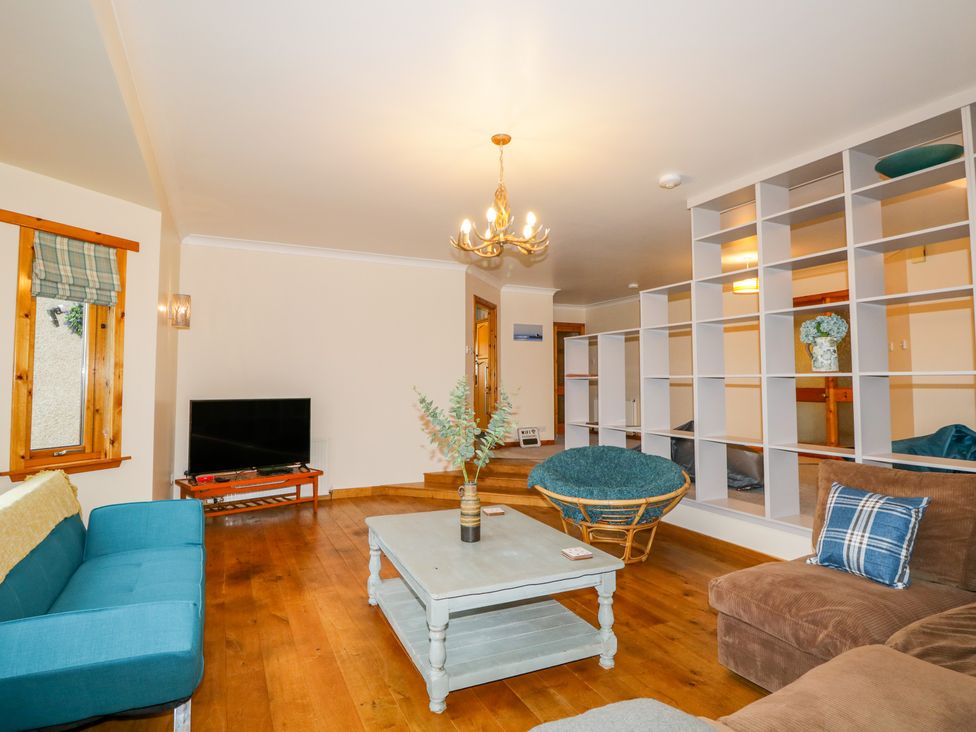 A living room with a blue sofa a brown chair a wooden coffee table a television and open shelving at Ptarmigan in Carrbridge