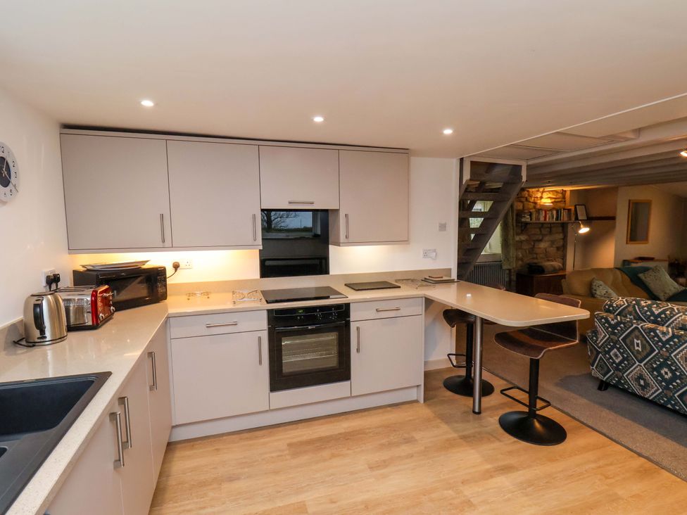 A kitchen with white cabinets a toaster microwave kettle oven and two bar stools at Orchard Cottage in Robin Hoods Bay