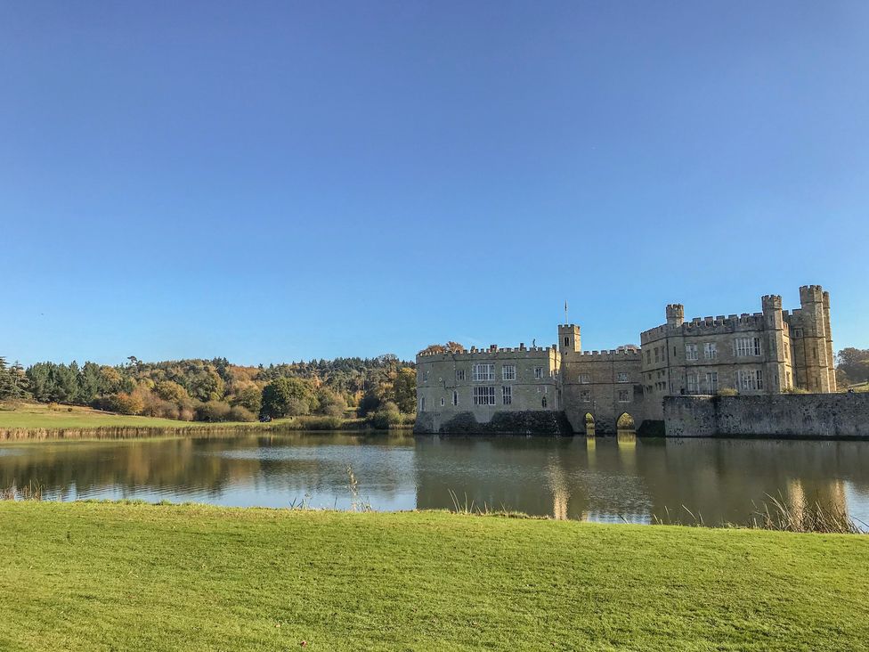 A historic castle surrounded by a moat with green grass and trees under a clear blue sky at The Oast in Leeds Village near Hollingbourne