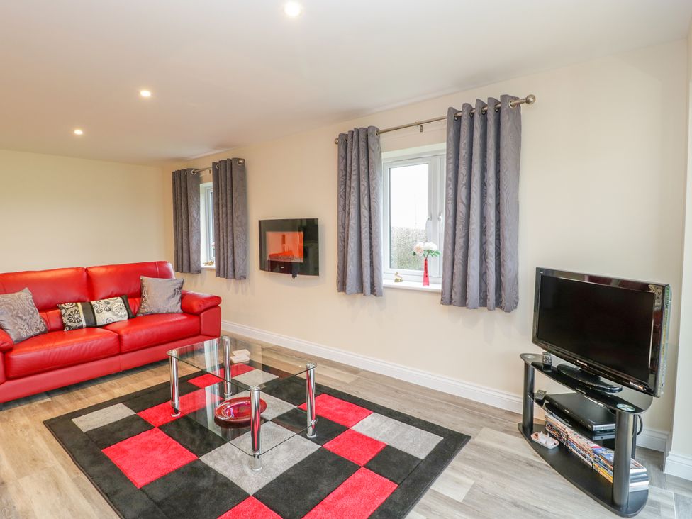 A living room with a red sofa glass coffee table and television on a stand at The Donkey Shed in Sherborne