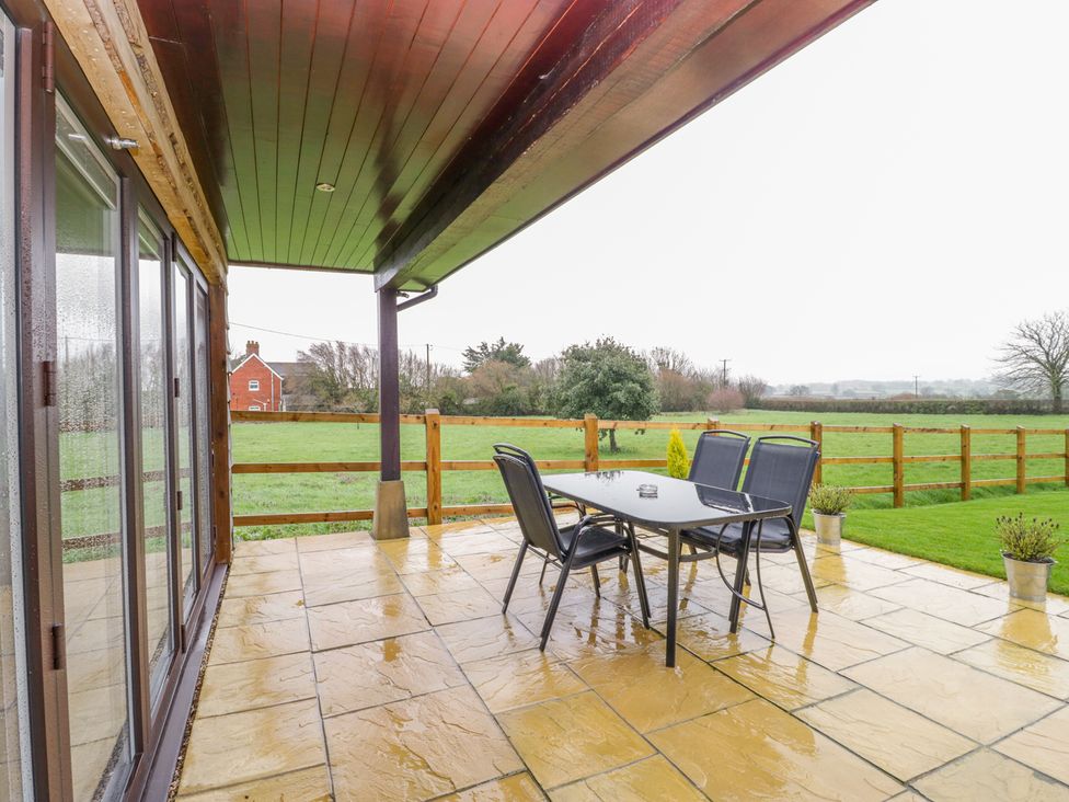 A covered patio with a glass table and four chairs overlooking a fenced grassy field at The Donkey Shed in Sherborne