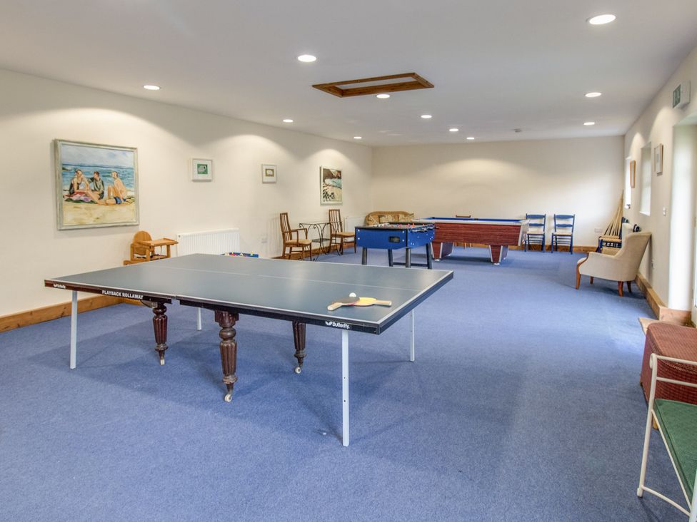 A game room with a ping pong table foosball table and pool table with chairs along the walls at Churn House in Dewlish