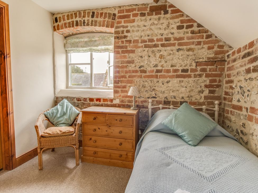 A bedroom with a bed a wooden dresser a wicker chair with cushions and a window at Manor Farm Barn in Dewlish