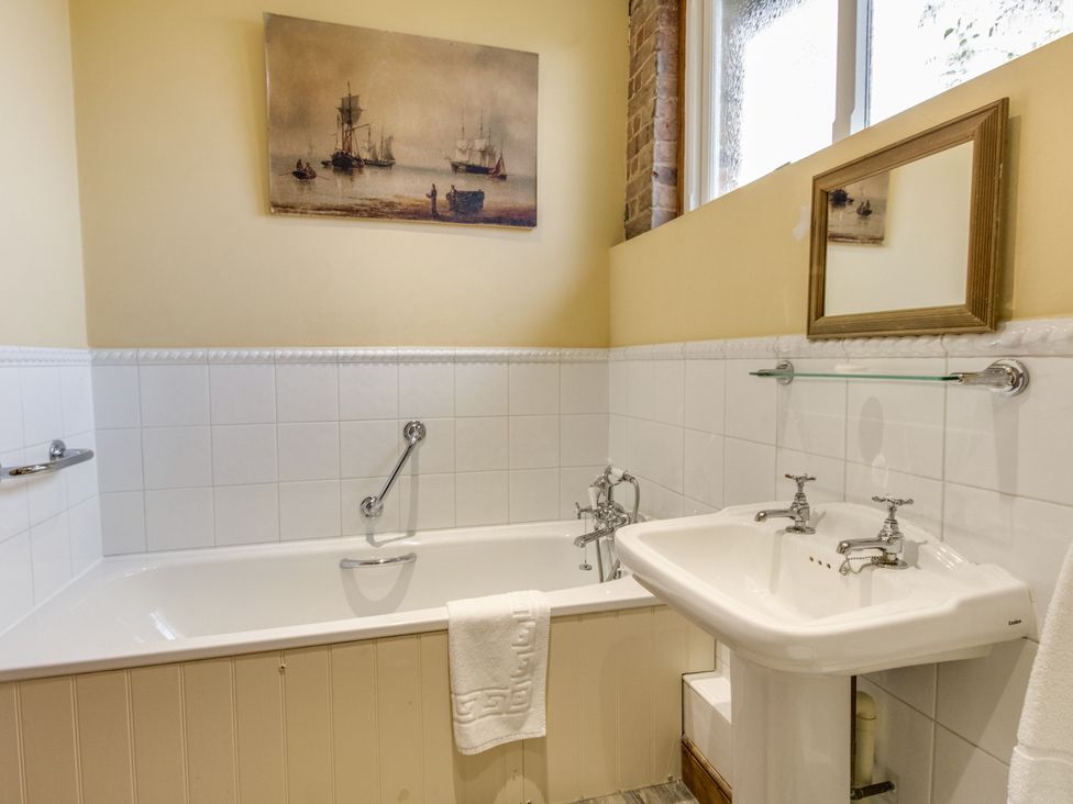 A bathroom with a bathtub a sink a small mirror and a painting on the wall at Manor Farm Barn in Dewlish