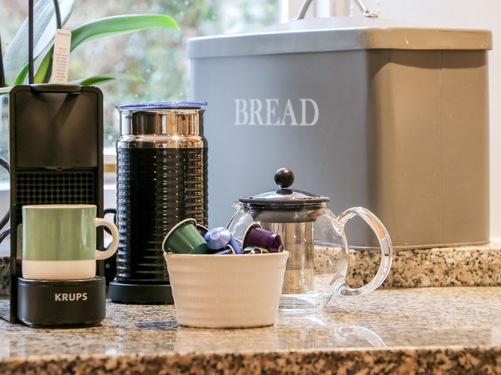 A kitchen counter with a coffee machine cup milk frother teapot container with coffee pods and a bread box at Court Prior Cottage in Cornworthy