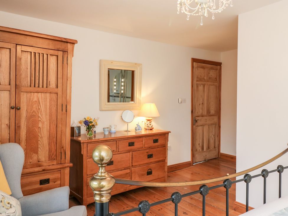 A bedroom with wooden wardrobe wooden dresser mirror armchair and metal bed frame at Court Prior Cottage in Cornworthy