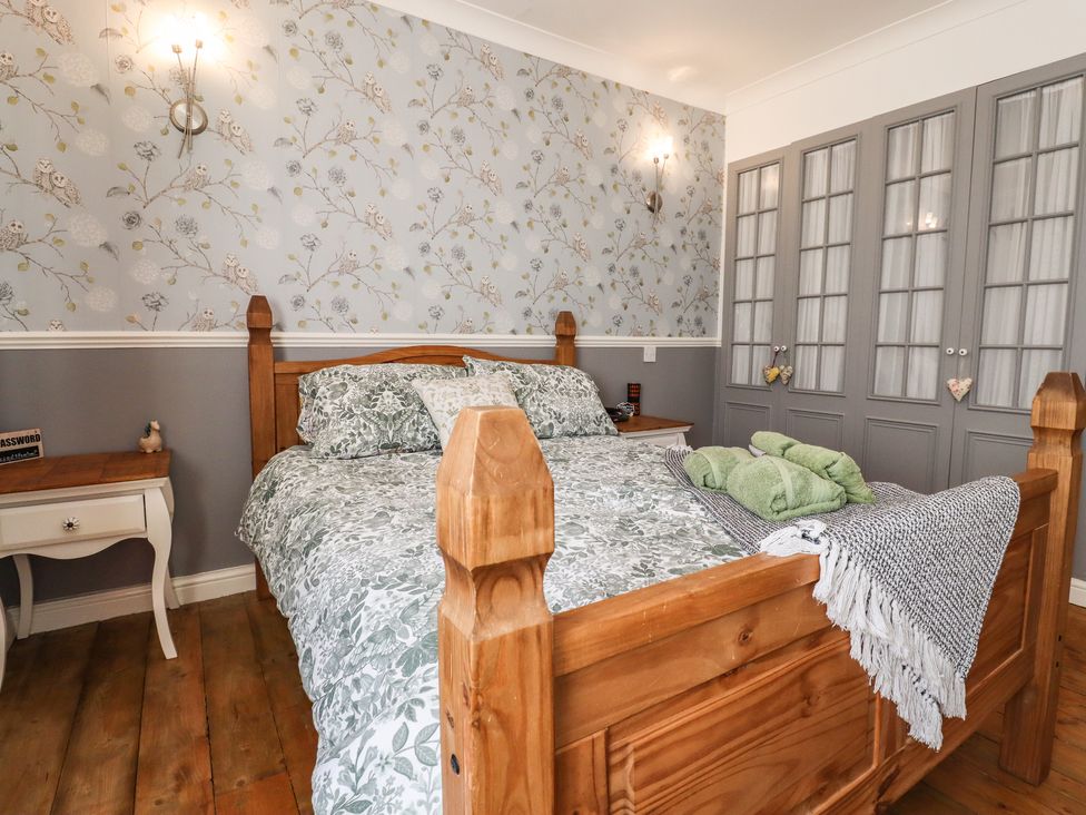 A bedroom with a wooden bed and gray floral bedding next to white bedside tables and gray wardrobes at Bay Cosy Pevensey Bay